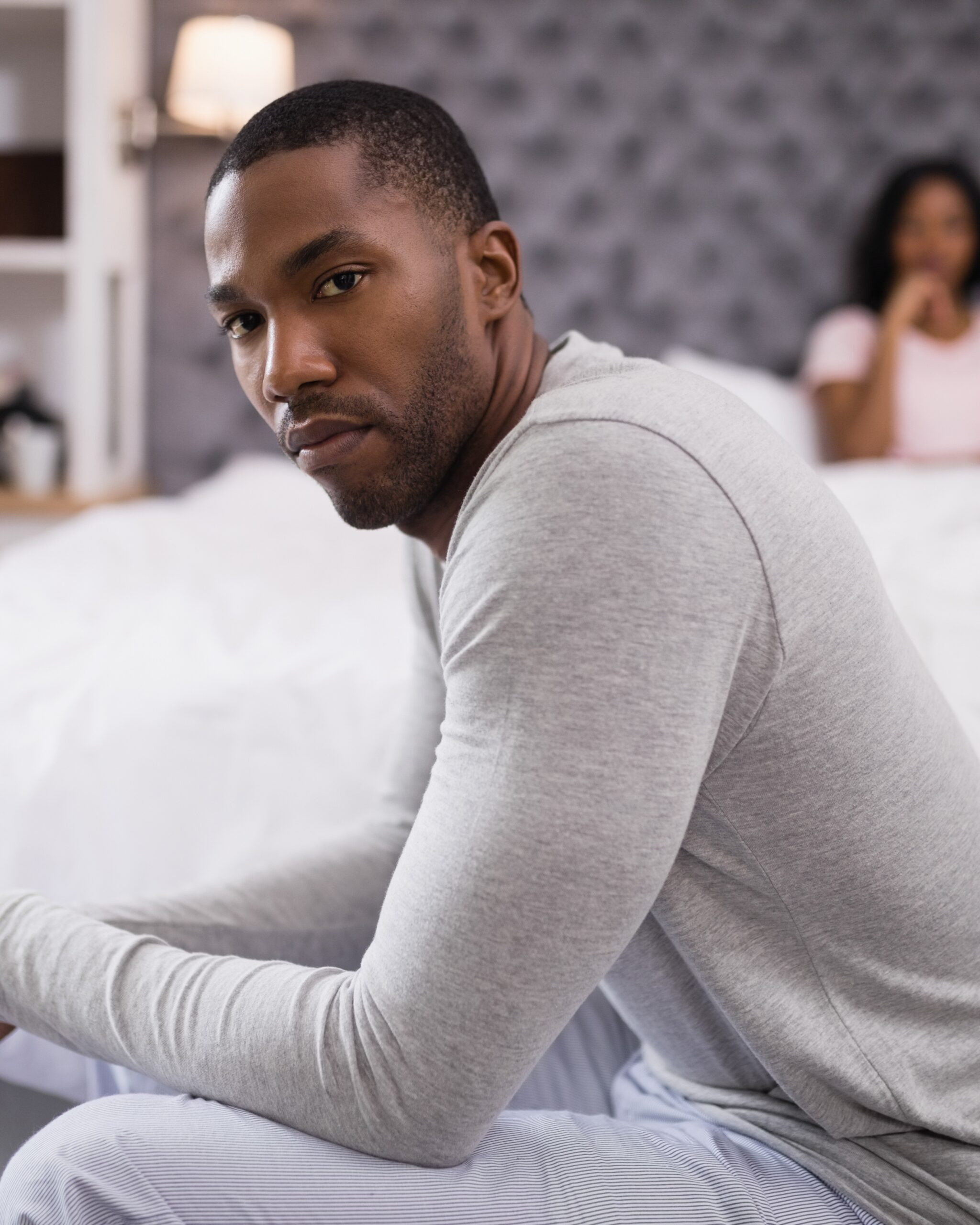 Portrait of young man siting while woman resting on bed at home