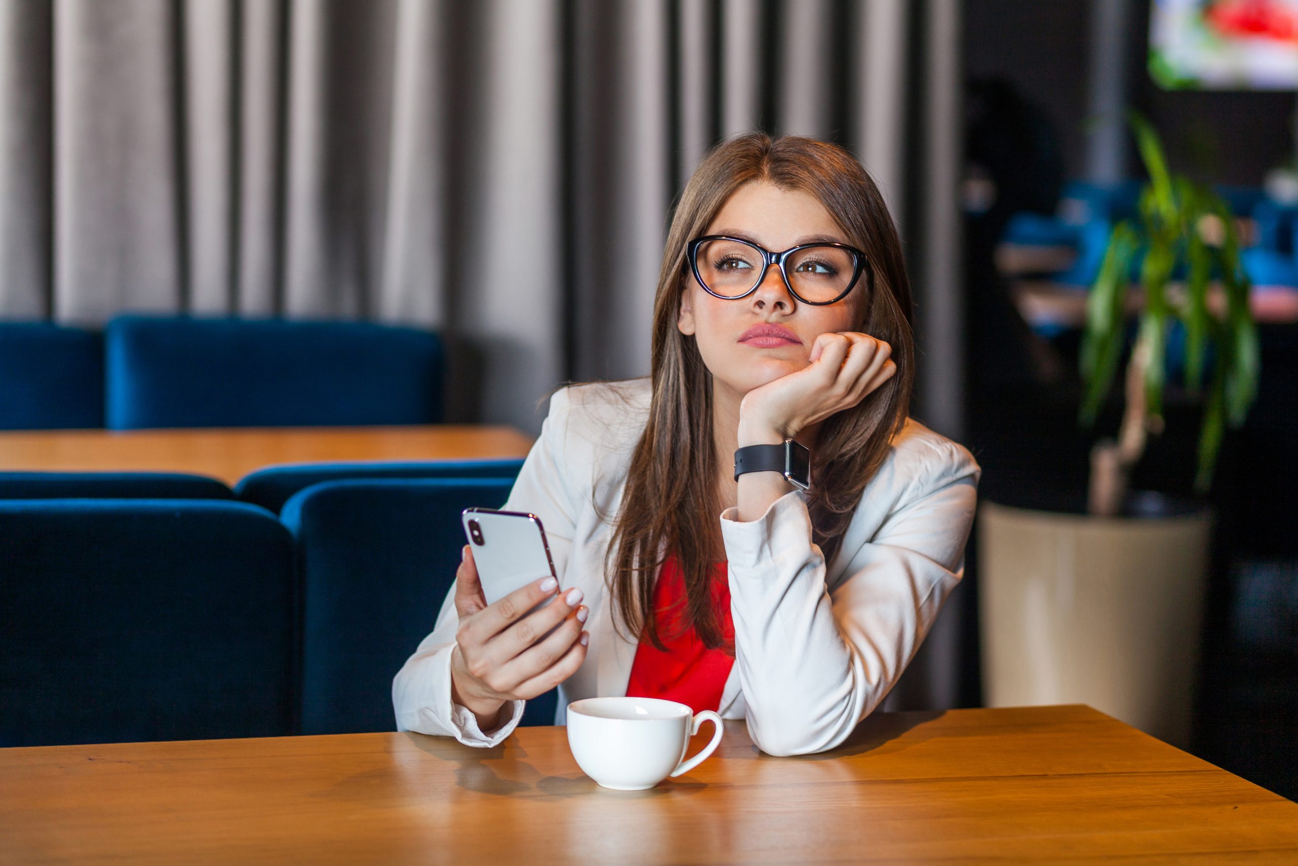 Young woman student or business person with glasses and a mobile phone thinking